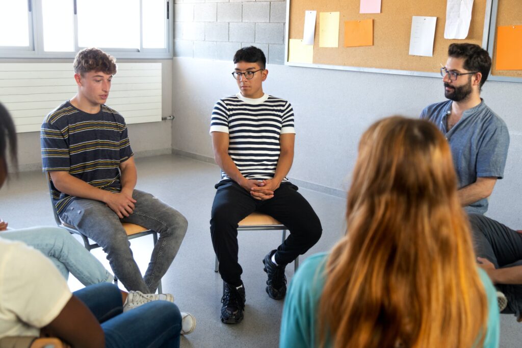 Students sitting in circle sharing problems with classmates and teacher. High school support group.